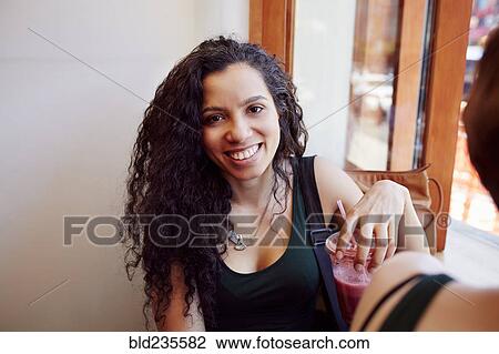 Stock Image - Smiling Black woman drinking smoothie in cafe. Fotosearch