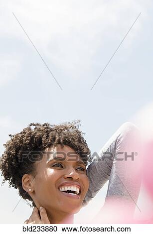 Stock Image - Smiling Black woman rubbing neck outdoors. Fotosearch