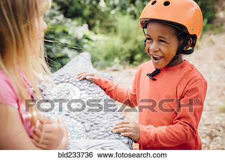 Smiling boy wearing helmet talking to girl on bench View Large Photo Image Stock Photograph - Smiling boy wearing helmet talking to girl on bench. Fotosearch