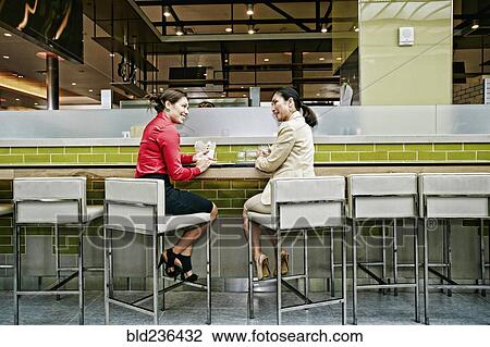 Stock Image - Smiling businesswomen talking in food court. Fotosearch