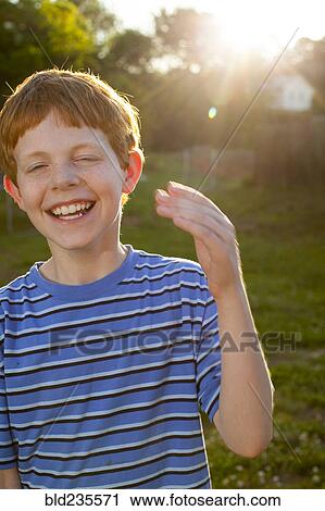 Stock Image - Smiling Caucasian boy laughing in sunny backyard. Fotosearch
