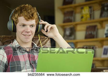 Picture - Smiling Caucasian boy listening to laptop with headphones. Fotosearch