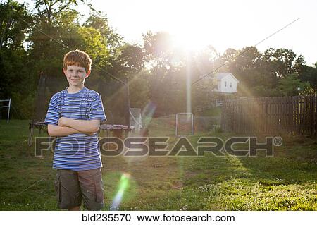 Stock Image - Smiling Caucasian boy standing in sunny backyard. Fotosearch