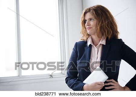 Stock Image - Smiling Caucasian businesswoman holding digital tablet near window. Fotosearch