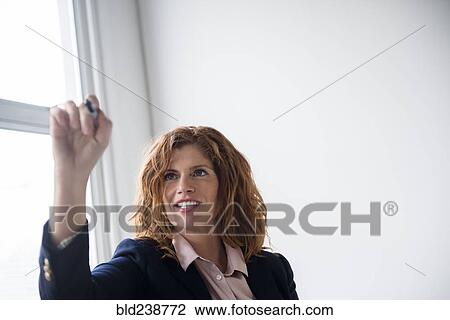 Stock Image - Smiling Caucasian businesswoman writing on glass wall with marker. Fotosearch