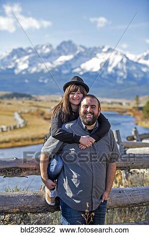 Stock Image - Smiling Caucasian couple posing at wooden fence near river. Fotosearch