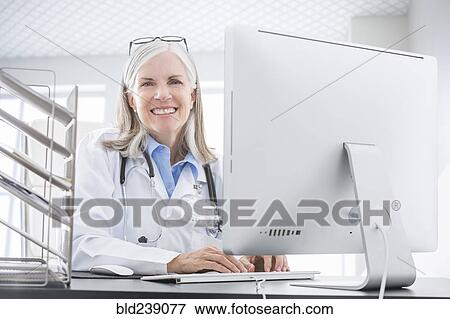 Stock Photo - Smiling Caucasian doctor using computer at desk. Fotosearch