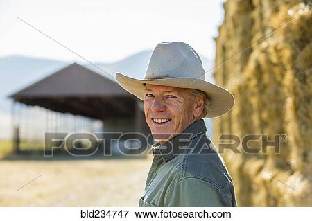 Stock Photo - Smiling Caucasian farmer near stacks of hay. Fotosearch