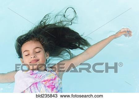 Stock Image - Smiling Caucasian girl floating in swimming pool. Fotosearch