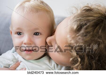 Stock Image - Smiling Caucasian girl kissing baby brother on cheek. Fotosearch