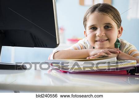 Stock Photograph - Smiling Caucasian girl leaning on notebooks at desk. Fotosearch