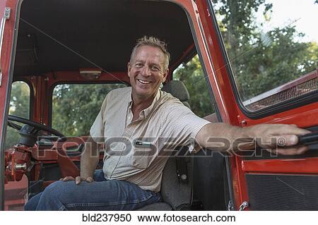 Stock Image - Smiling Caucasian man holding door of tractor. Fotosearch