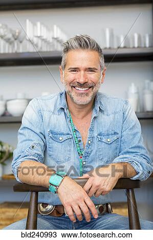 Smiling Caucasian man leaning on chair in store View Large Photo Image Stock Image - Smiling Caucasian man leaning on chair in store. Fotosearch