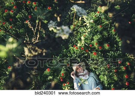 Stock Image - Smiling Caucasian woman laying in flowers. Fotosearch