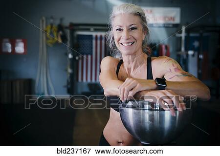 Stock Photo - Smiling Caucasian woman leaning on bowl in gymnasium. Fotosearch
