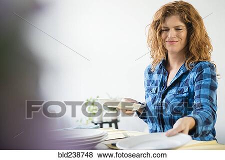 Stock Photo - Smiling Caucasian woman setting table for meal. Fotosearch