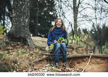 Smiling Caucasian woman sitting on tree root holding branch View Large Photo Image Stock Image - Smiling Caucasian woman sitting on tree root holding branch. Fotosearch
