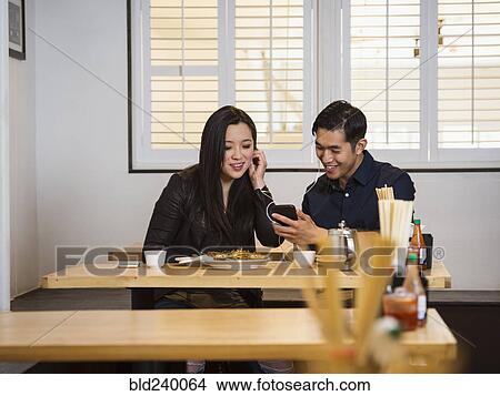 Smiling Chinese couple listening to cell phone in restaurant View Large Photo Image Picture - Smiling Chinese couple listening to cell phone in restaurant. Fotosearch