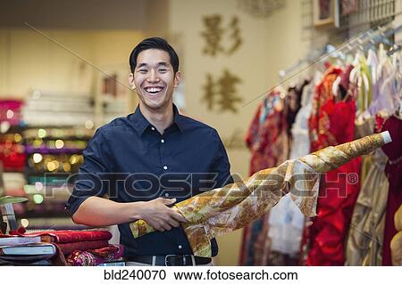Stock Image - Smiling Chinese man posing with fabric in store. Fotosearch