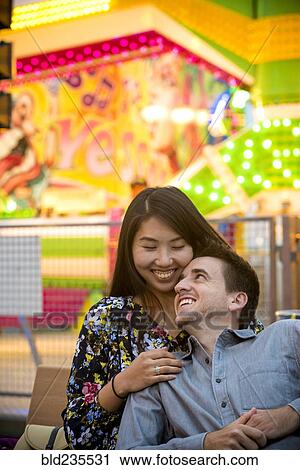 Smiling couple cuddling on bench in amusement park View Large Photo Image Stock Image - Smiling couple cuddling on bench in amusement park. Fotosearch