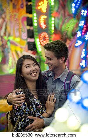 Stock Image - Smiling couple hugging in amusement park. Fotosearch