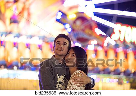 Stock Photograph - Smiling couple hugging in amusement park. Fotosearch