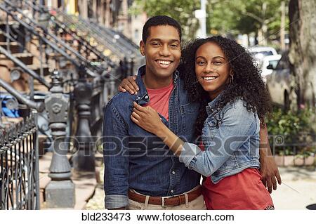 Stock Image - Smiling couple hugging on city sidewalk. Fotosearch