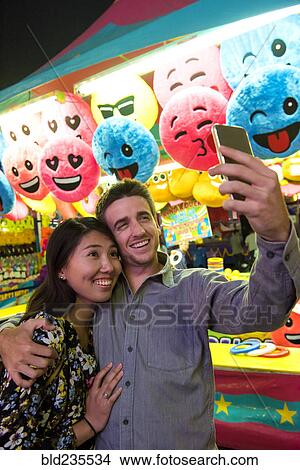 Smiling couple posing for cell phone selfie in amusement park View Large Photo Image Picture - Smiling couple posing for cell phone selfie in amusement park. Fotosearch