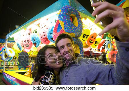 Smiling couple posing for cell phone selfie in amusement park View Large Photo Image Stock Photography - Smiling couple posing for cell phone selfie in amusement park. Fotosearch