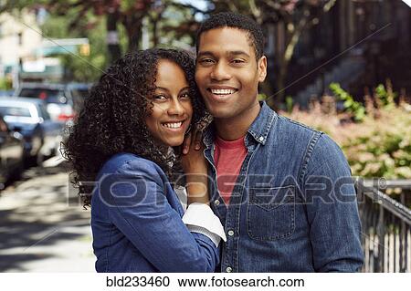 Stock Image - Smiling couple posing on city sidewalk. Fotosearch