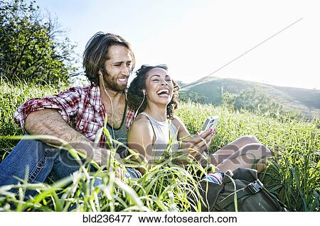 Smiling couple sitting on hill listening to cell phone View Large Photo Image Stock Photo - Smiling couple sitting on hill listening to cell phone. Fotosearch