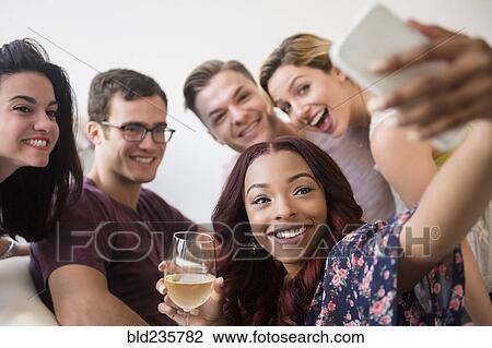 Stock Image - Smiling friends posing for cell phone selfie. Fotosearch