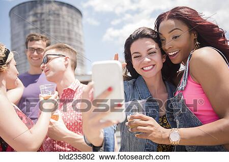 Stock Image - Smiling friends posing for cell phone selfie outdoors. Fotosearch