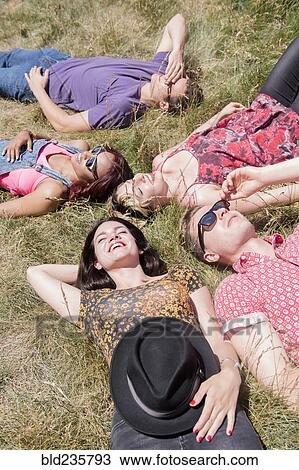 Stock Image - Smiling friends relaxing in sunny grass field. Fotosearch