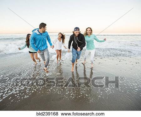 Stock Photo - Smiling friends running on beach. Fotosearch
