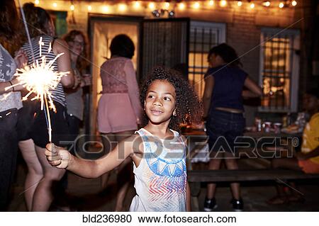 Smiling girl holding burning sparkler at backyard party View Large Photo Image Stock Image - Smiling girl holding burning sparkler at backyard party. Fotosearch