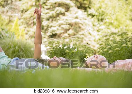 Smiling girls laying in grass pointing up View Large Photo Image Stock Photograph - Smiling girls laying in grass pointing up. Fotosearch