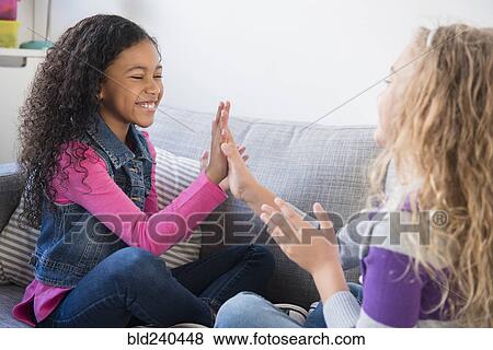 Stock Photo - Smiling girls playing clapping game on sofa. Fotosearch