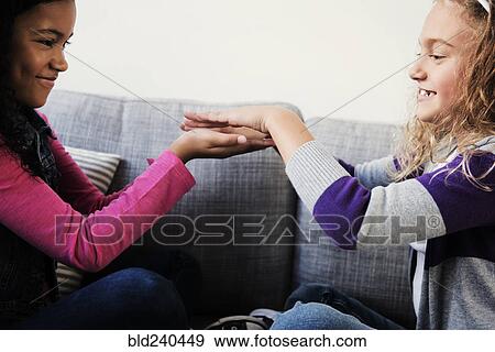 Stock Photo - Smiling girls playing game with hands on sofa. Fotosearch