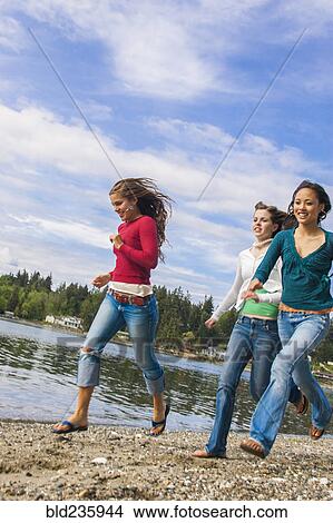 Picture - Smiling girls running on rocky beach. Fotosearch