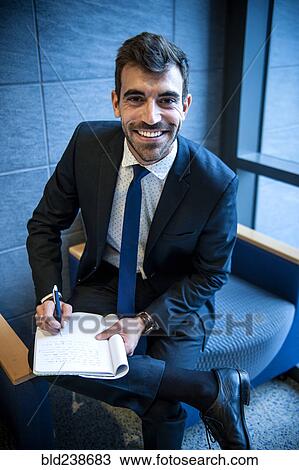 Stock Image - Smiling Hispanic businessman writing on notepad in office lounge. Fotosearch