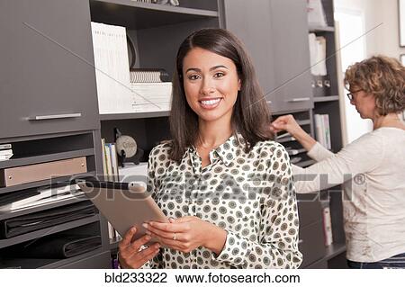 Stock Image - Smiling Hispanic businesswoman holding digital tablet near co-worker. Fotosearch