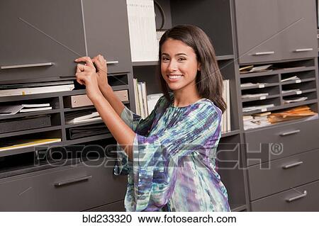 Smiling Hispanic businesswoman opening office cabinet View Large Photo Image Stock Image - Smiling Hispanic businesswoman opening office cabinet. Fotosearch