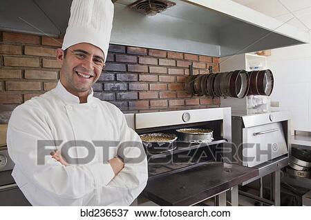 Stock Photo - Smiling Hispanic chef posing near cheesecakes in oven. Fotosearch