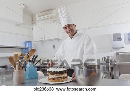 Stock Photo - Smiling Hispanic chef spreading icing on cake. Fotosearch