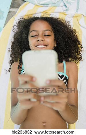 Stock Image - Smiling Hispanic girl texting on cell phone at swimming pool. Fotosearch