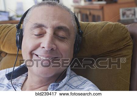 Stock Photo - Smiling Hispanic man listening to headphones. Fotosearch