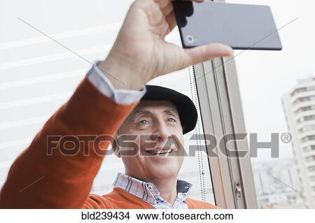 Picture - Smiling Hispanic man posing for cell phone selfie. Fotosearch
