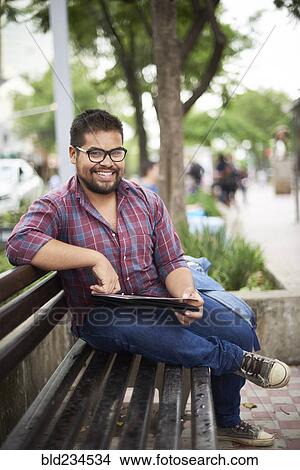 Smiling Hispanic man sitting on bench reading brochure View Large Photo Image Picture - Smiling Hispanic man sitting on bench reading brochure. Fotosearch