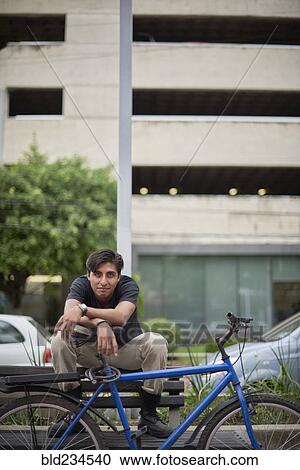 Smiling Hispanic man sitting on bench with bicycle View Large Photo Image Stock Image - Smiling Hispanic man sitting on bench with bicycle. Fotosearch